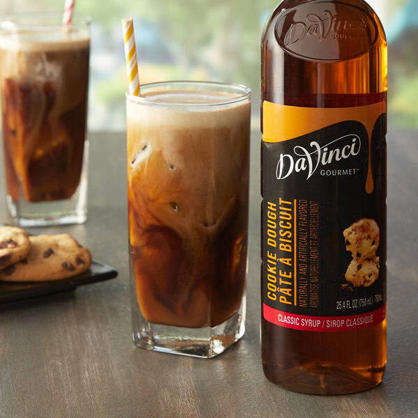 A bottle of DaVinci Gourmet Classic Cookie Dough flavoring syrup next to a glass of brown liquid.