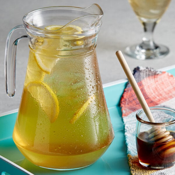 A pitcher of lemonade with DaVinci Gourmet Classic Honey Sweetener Syrup on a table with lemons and a spoon.