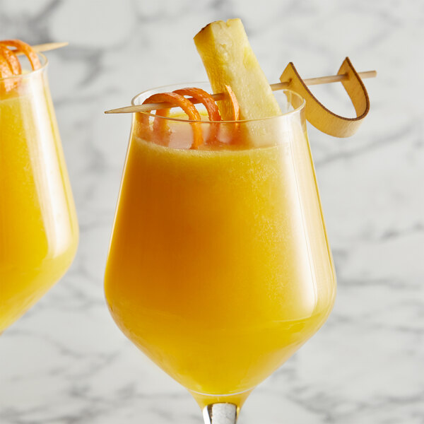A glass of DaVinci Gourmet Classic Pineapple flavored orange juice with a straw and an orange slice.