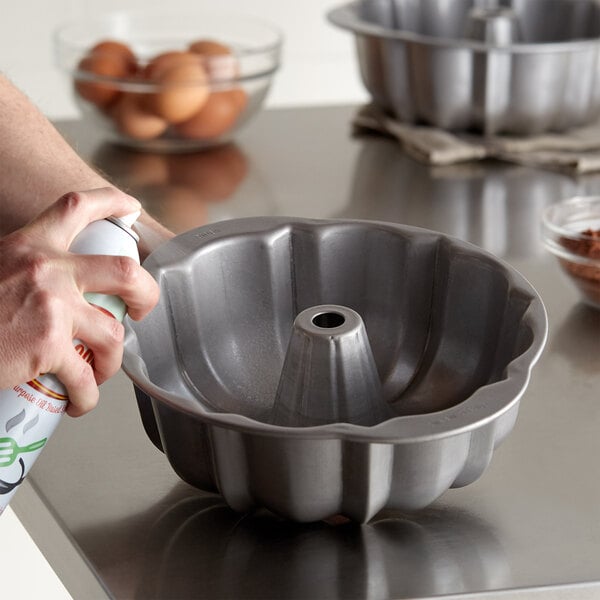 A hand spraying a Chicago Metallic fluted bundt cake pan with a spray bottle.