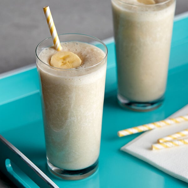 Two glasses of milkshake with banana slices and straws on a tray.