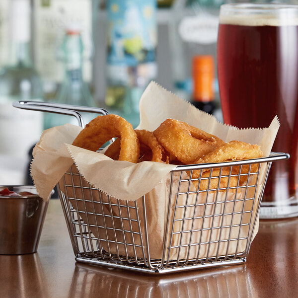 A chrome square mini fry basket filled with fried onion rings on a table in a restaurant.
