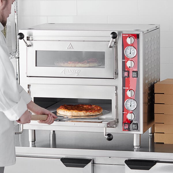 A man in a white coat baking pizza in an Avantco double deck countertop pizza oven.