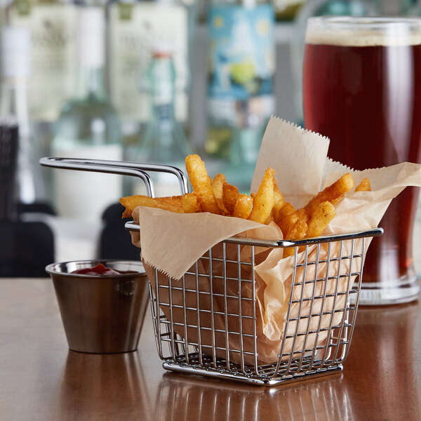 A chrome rectangular mini fry basket filled with fries in a paper bag with a glass of beer.