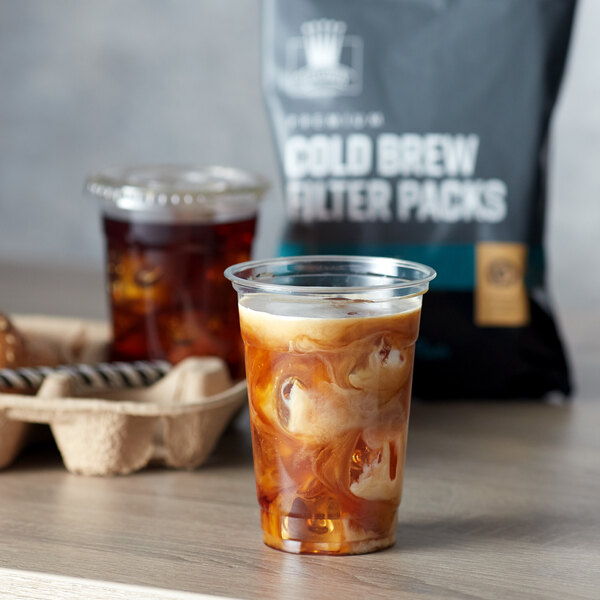 A cup of iced coffee next to a Crown Beverages Cold Brew Filter Pack bag.