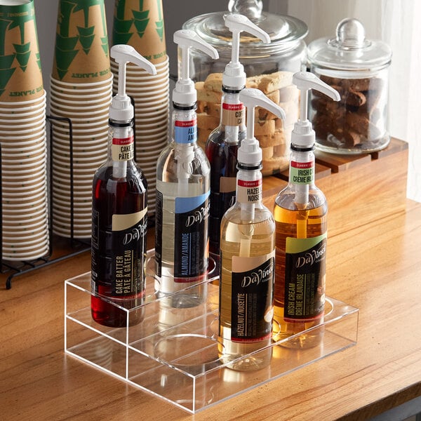 A Choice 2 Tier syrup bottle organizer holding glass bottles of liquid on a table.