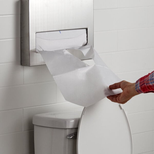 A hand holding a Lavex half fold paper toilet seat cover over a toilet.