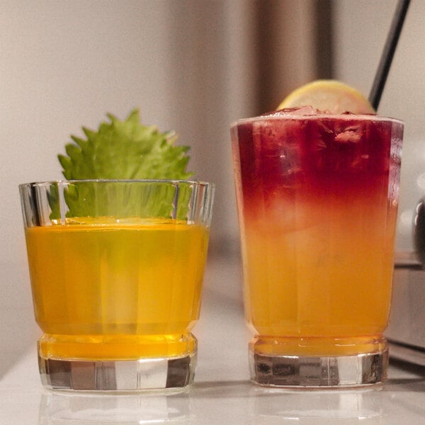 Two Chef & Sommelier highball glasses with yellow drinks and garnishes on a counter.