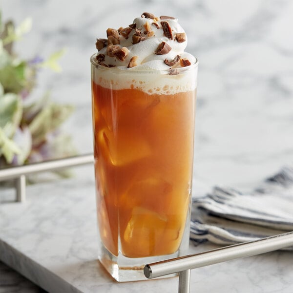 A glass of liquid with ice cubes and whipped cream and nuts with DaVinci Gourmet Sugar Free English Toffee Flavoring Syrup.