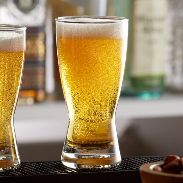 Two Libbey pilsner glasses of beer on a bar counter.