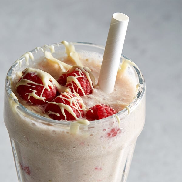 A glass of milkshake with a straw, raspberries, and DaVinci Gourmet Sugar Free White Chocolate Flavoring Syrup.
