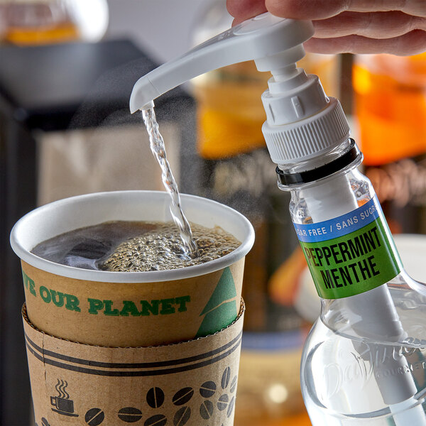 A hand pouring DaVinci Gourmet Sugar Free Peppermint Flavoring Syrup into a cup of coffee.