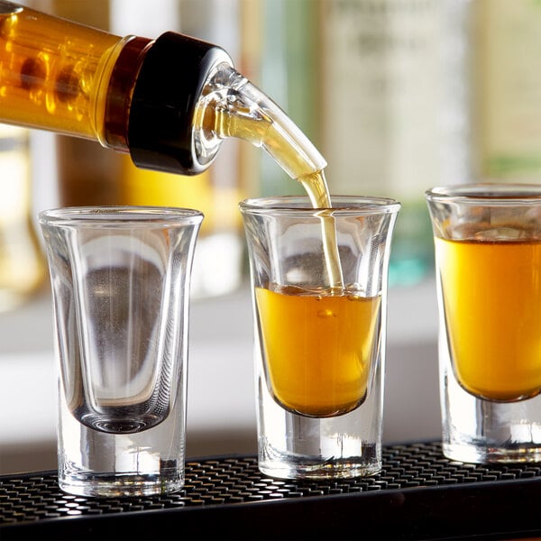A person pouring brown liquor into a Libbey shot glass.