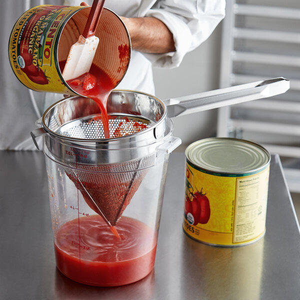 A person using a Choice Coarse China Cap Strainer to pour tomato sauce into a container.