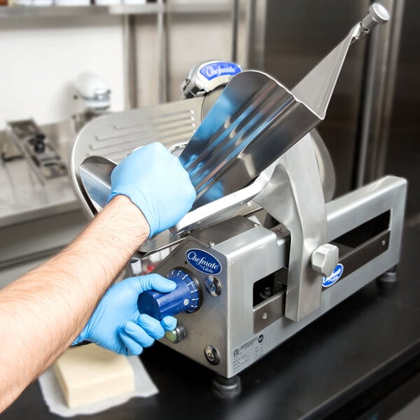 A person using a Globe Chefmate manual meat slicer to cut meat on a counter while wearing blue gloves.