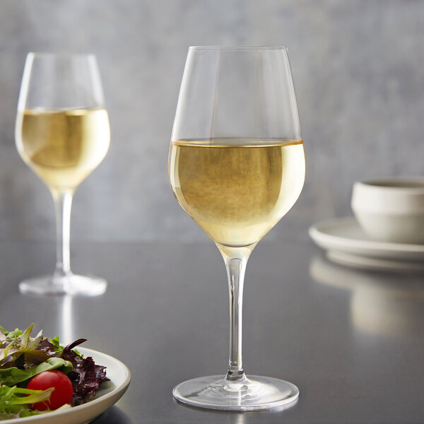 A Stolzle Exquisit white wine glass filled with yellow liquid next to a plate of salad.