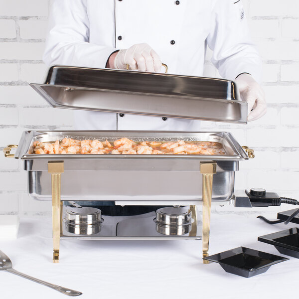 A chef using a Vollrath stainless steel chafer fuel holder to prepare food in a large chafing dish.