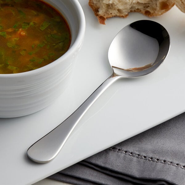 A bowl of soup and an Acopa Vernon stainless steel bouillon spoon on a plate.