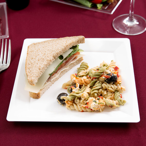 A WNA Comet white square plastic plate with a sandwich and pasta on it.