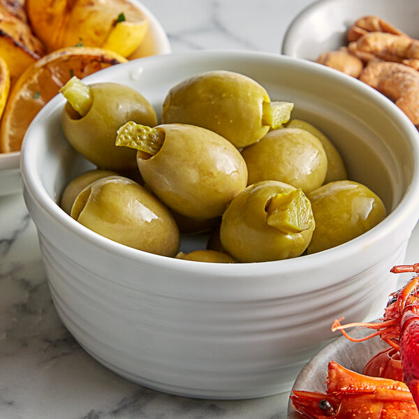 A bowl of green olives and other food on a table.