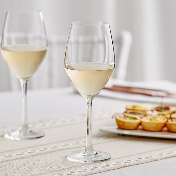 Two Acopa wine glasses filled with white wine on a table.