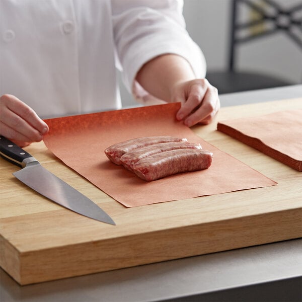 A person holding a piece of meat on a cutting board.