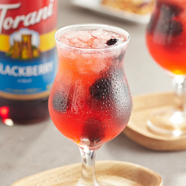 A glass of Torani blackberry syrup in red liquid with ice and blackberries.
