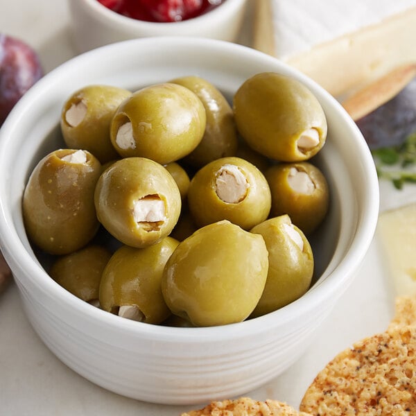 A white bowl of Belosa blue cheese stuffed green olives on a table with cheese and crackers.