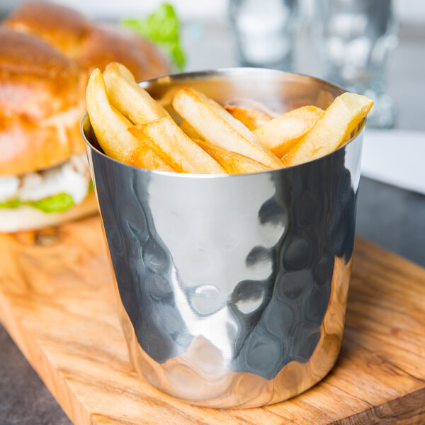 A silver American Metalcraft stainless steel cup filled with French fries on a cutting board.