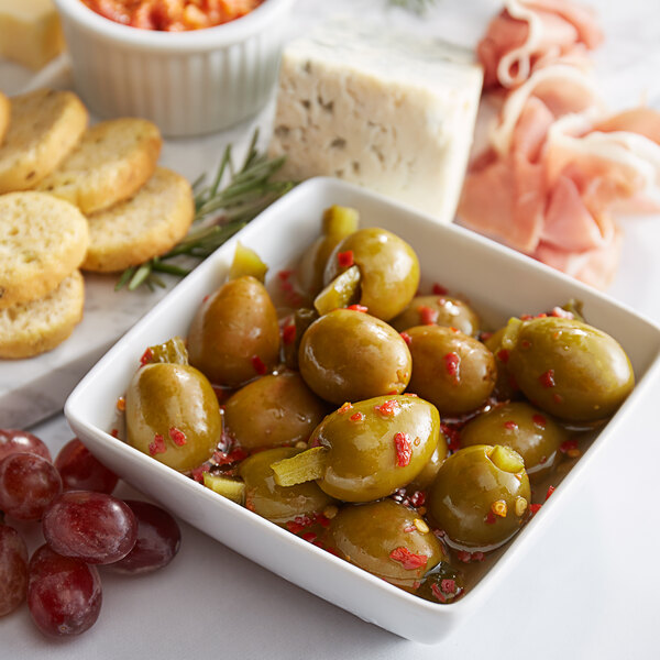 A bowl of Belosa sweet & spicy pickle stuffed green olives and grapes on a table.