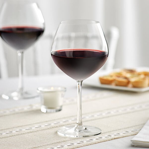 Two Acopa burgundy wine glasses filled with red wine on a table.