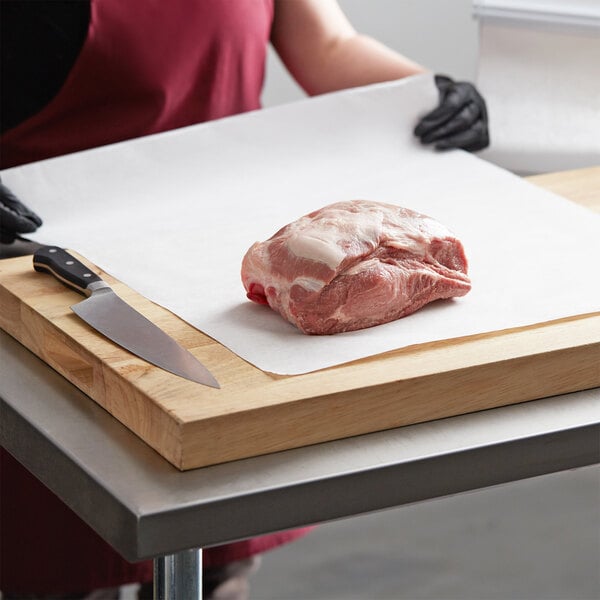 A person in a red shirt cutting meat on a white Choice True Butcher Paper-covered surface.