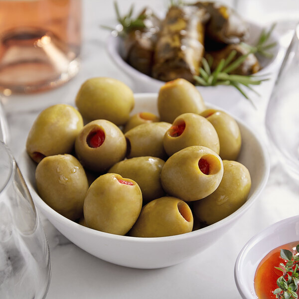 A bowl of Belosa sundried tomato stuffed green olives on a table with a glass of wine.