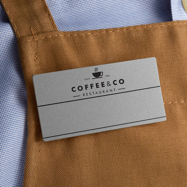 A customizable silver rectangle nametag on a brown apron.
