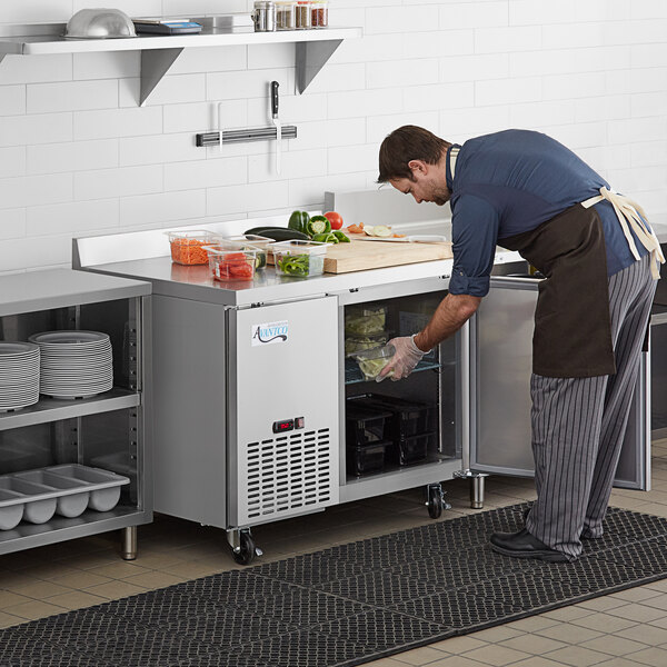 A man in a blue apron putting food in an Avantco worktop refrigerator.