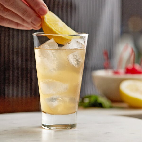 A person squeezing a lemon wedge into a Libbey highball glass of liquid with ice.