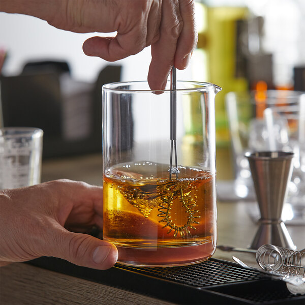 A person using a Fox Run mini whisk to stir a drink in a glass.