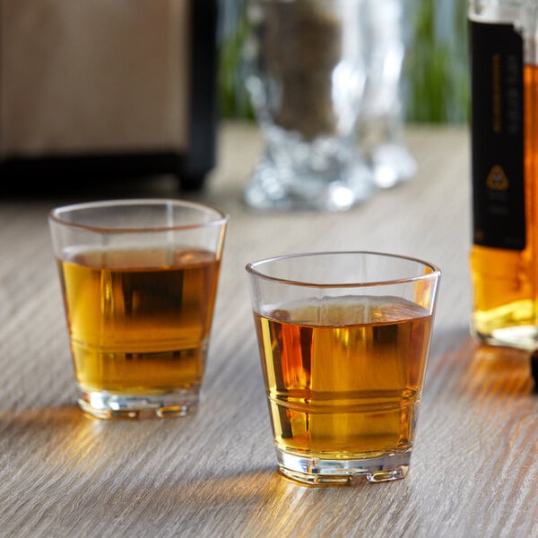 Two Libbey plastic stackable shot glasses filled with brown liquid on a table.