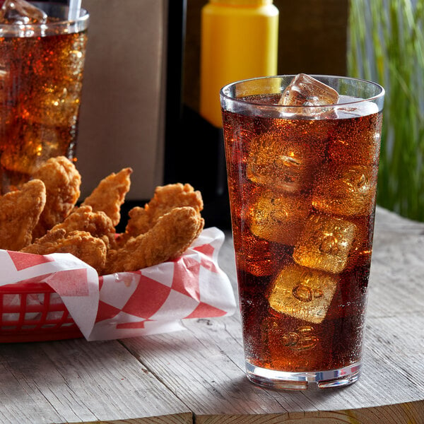 A close-up of a Libbey Tritan plastic mixing glass filled with cola and ice on a table with chicken strips.