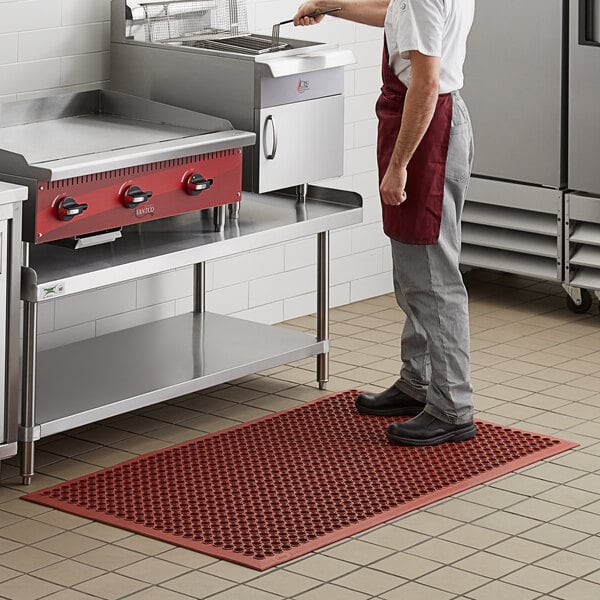 A man standing on a red Choice anti-fatigue floor mat in a kitchen.