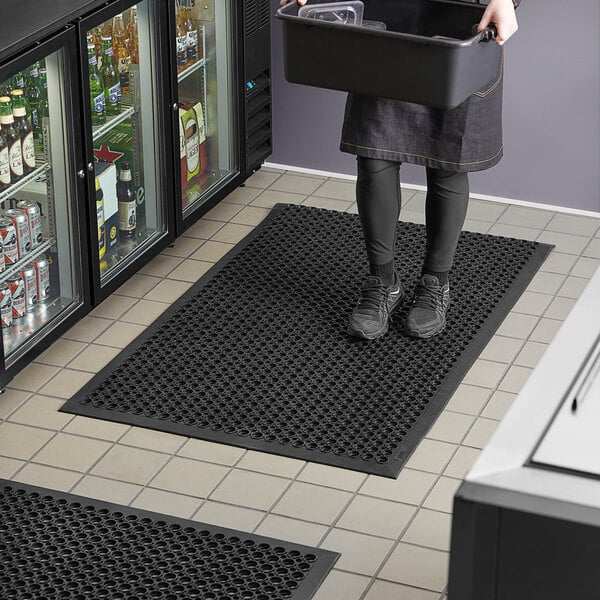 A woman standing on a black Lavex anti-fatigue floor mat in front of a refrigerator.