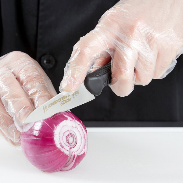 A hand in a plastic glove uses a Dexter-Russell DuoGlide paring knife to slice a red onion.