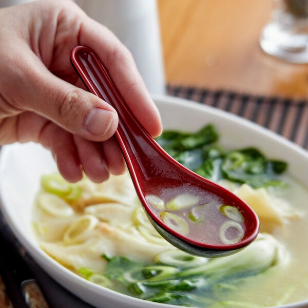 A person holding a red and black Thunder Group wonton soup spoon over a bowl of soup.