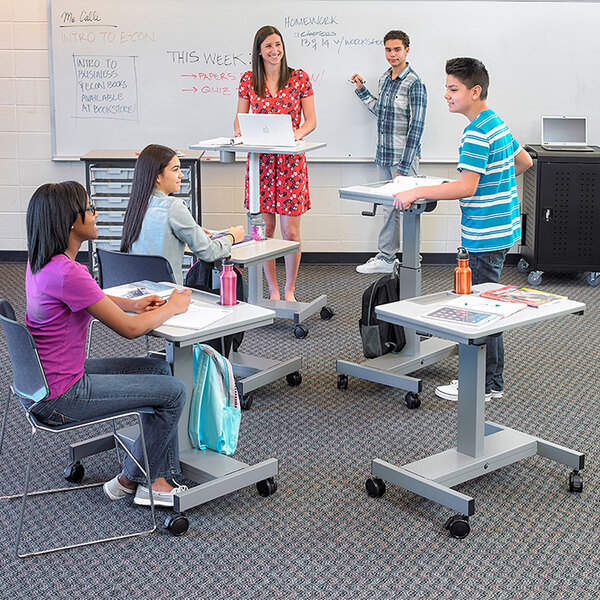 A group of students sitting at a Luxor adjustable height standing desk in a classroom.