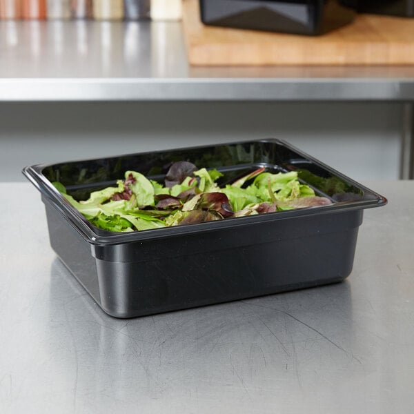 A black Cambro plastic food pan filled with lettuce on a counter.