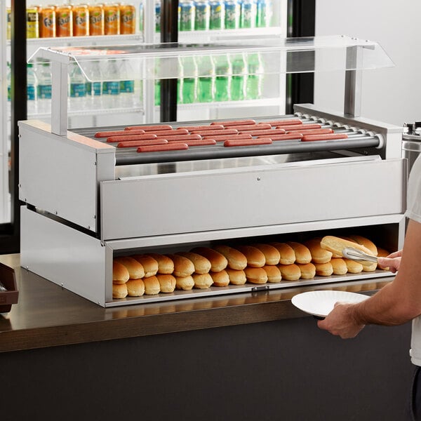 A man using an Avantco stainless steel bun cabinet to put hot dogs on a plate.