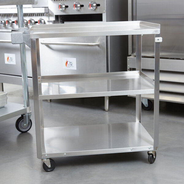 A Vollrath stainless steel utility cart with three shelves in a kitchen.