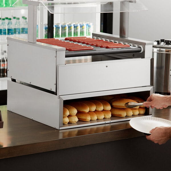 A person using an Avantco stainless steel bun cabinet to put hot dogs on a plate.