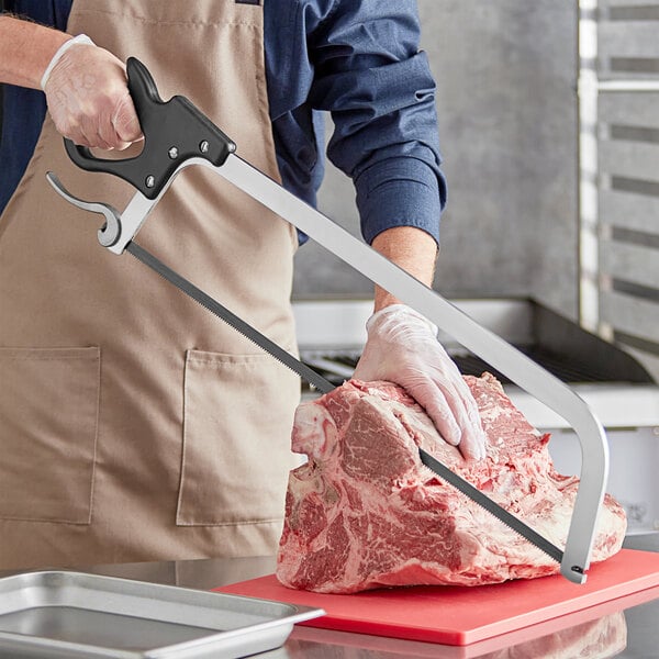 A hand using a Backyard Pro stainless steel hand meat saw to cut a piece of meat.