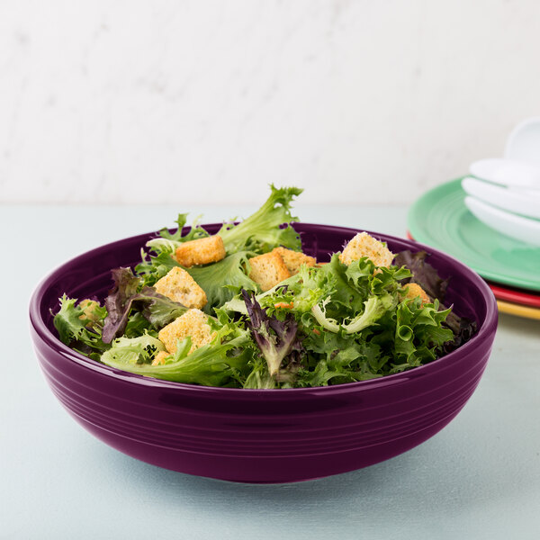 A Fiesta Mulberry china bistro bowl filled with salad on a table.